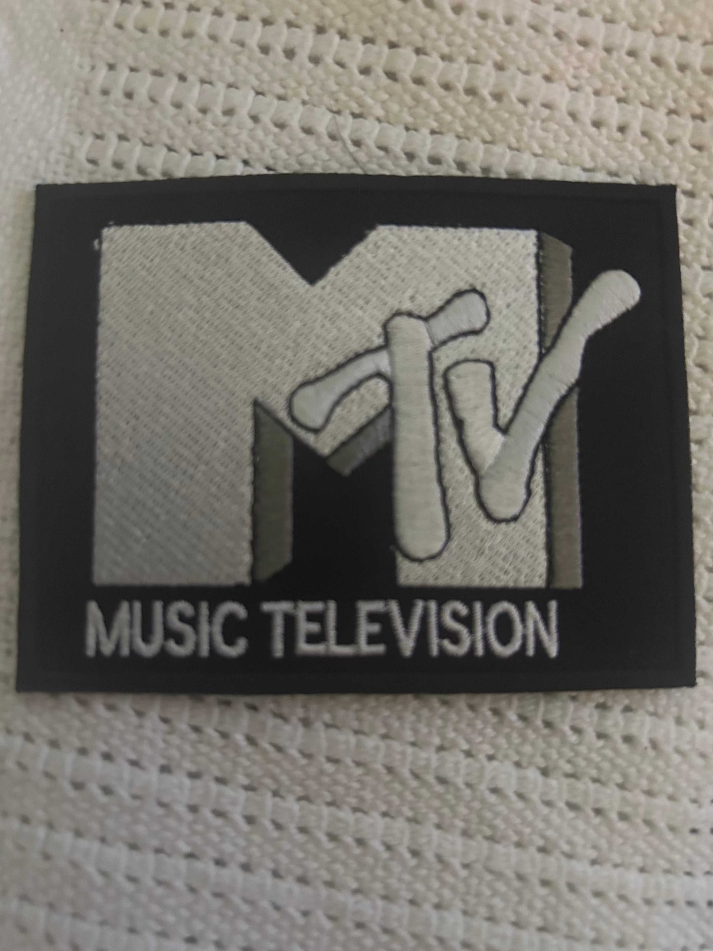 MTV embroidered patch featuring the iconic MTV logo and "Music Television" text in black, white, and gray colors on a textured fabric background