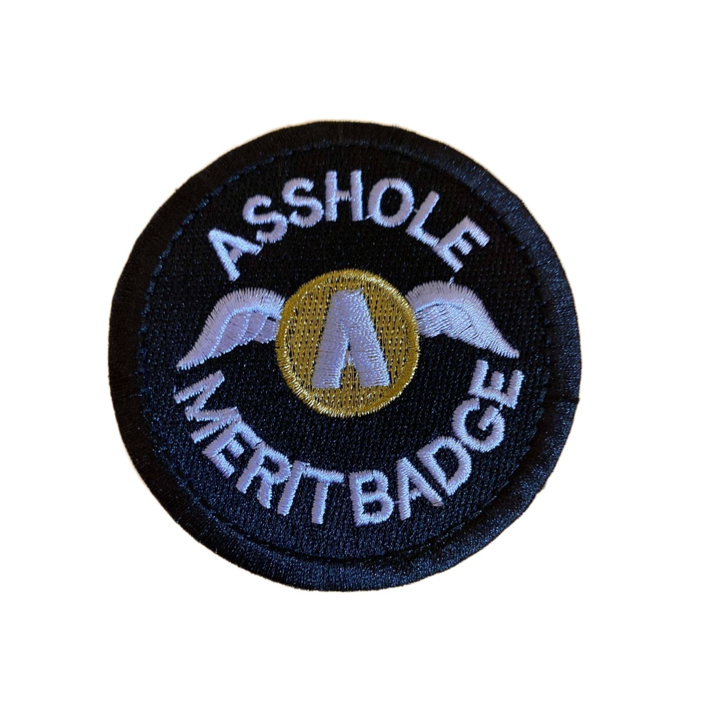 Round black merit badge with white text "Asshole Merit Badge" and a gold winged emblem in the center