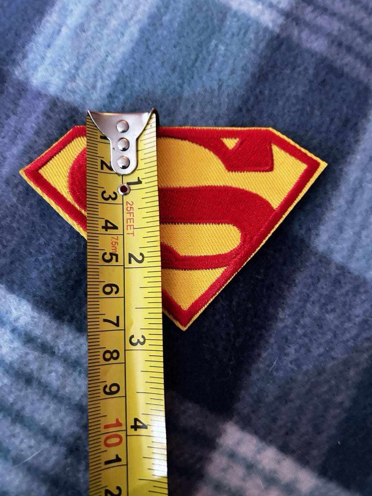 Vintage Superman embroidered iron-on patch with measuring tape showing size, 4.5" x 3", on a soft surface.