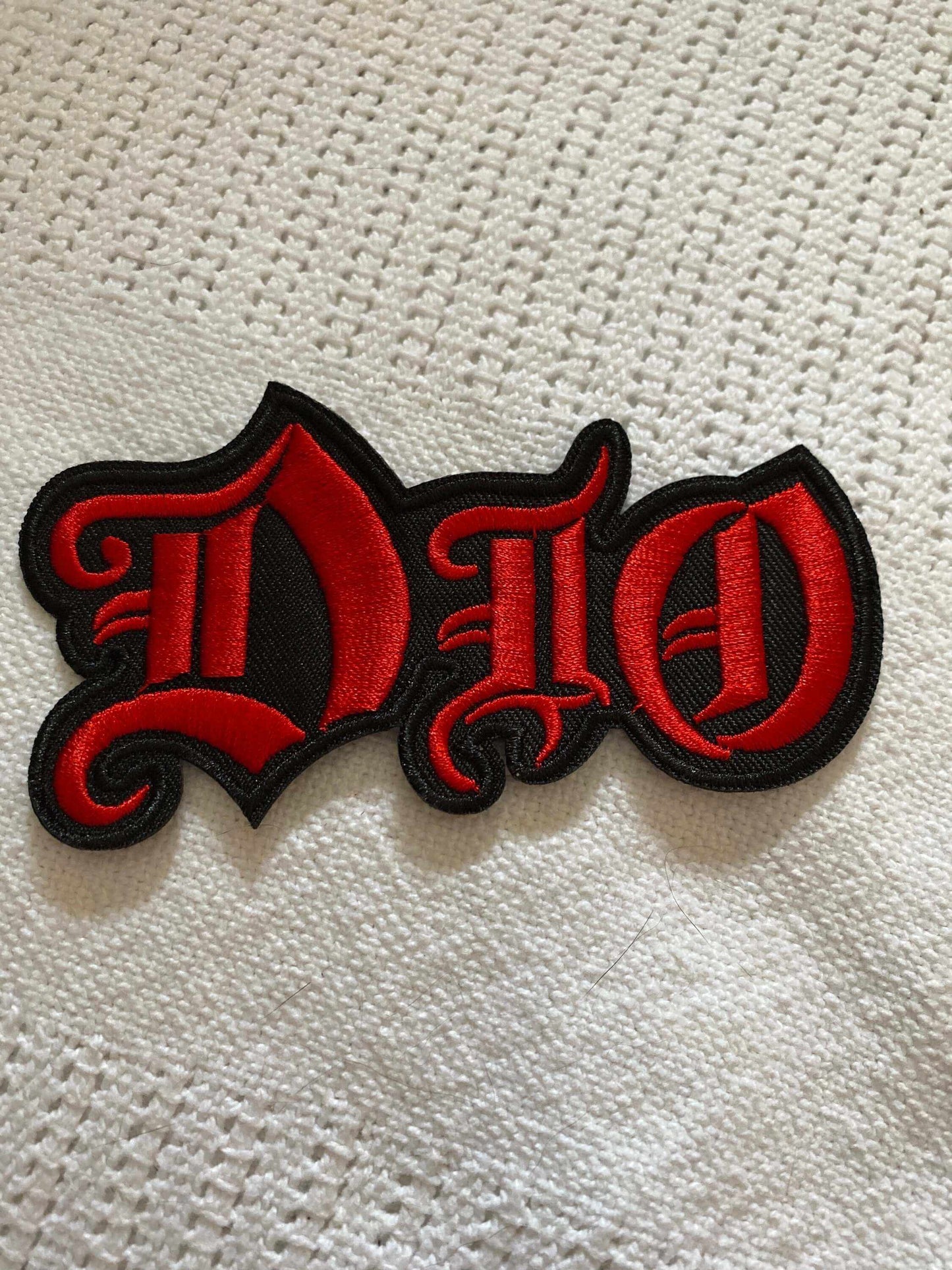 DIO rock band logo patch embroidered in red and black on white fabric background