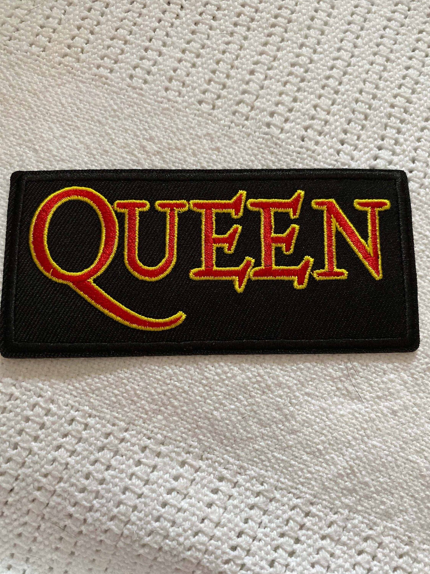 Queen rock band logo patch with bold yellow and red lettering on black background