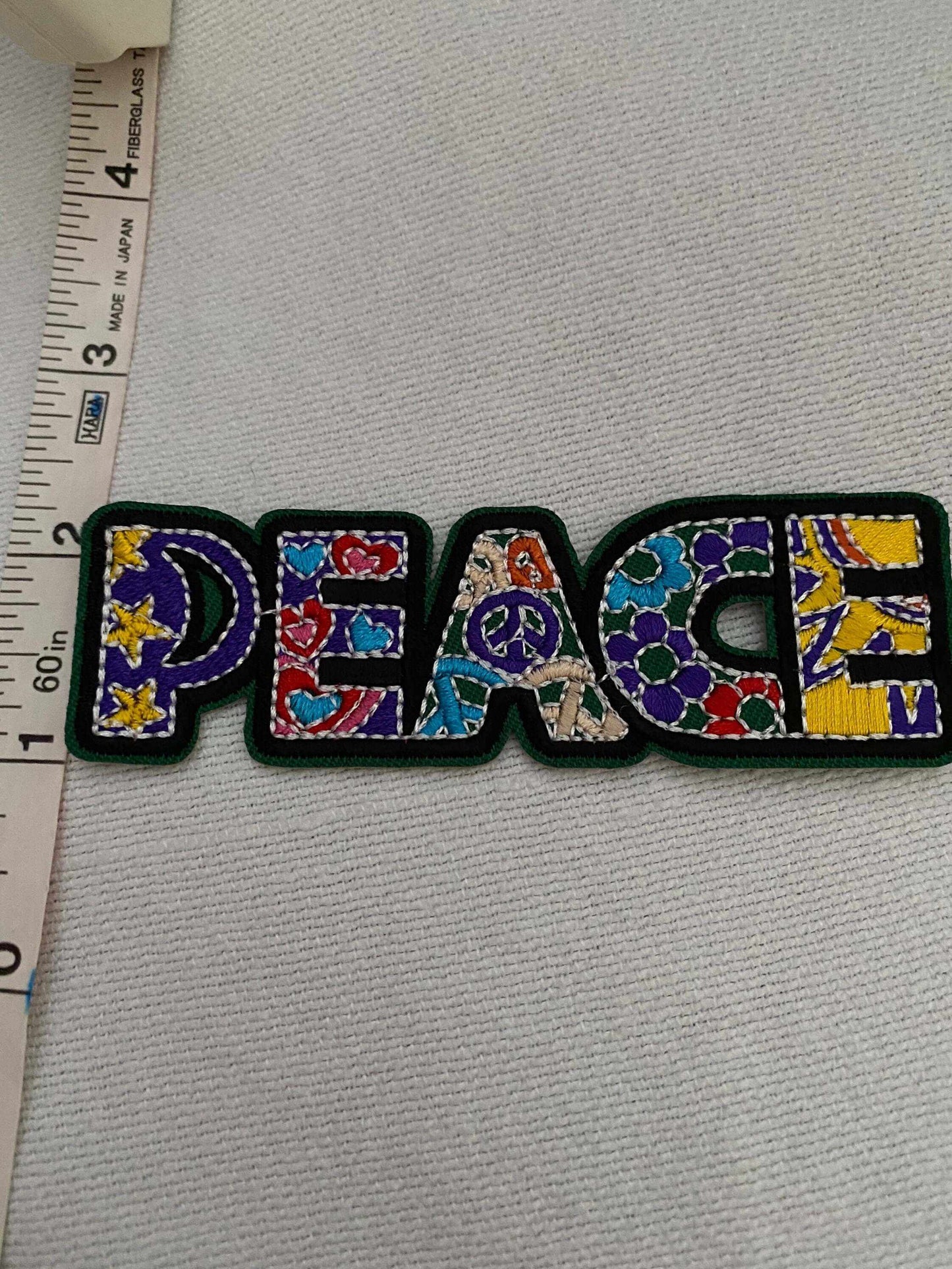 Colorful PEACE multicolored fabric patch with peace symbols and floral patterns, measuring about 4 inches wide.