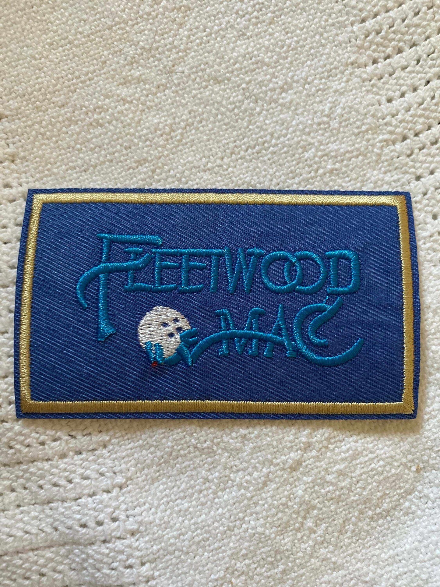 Blue embroidered Fleetwood Mac logo patch on white knitted fabric background