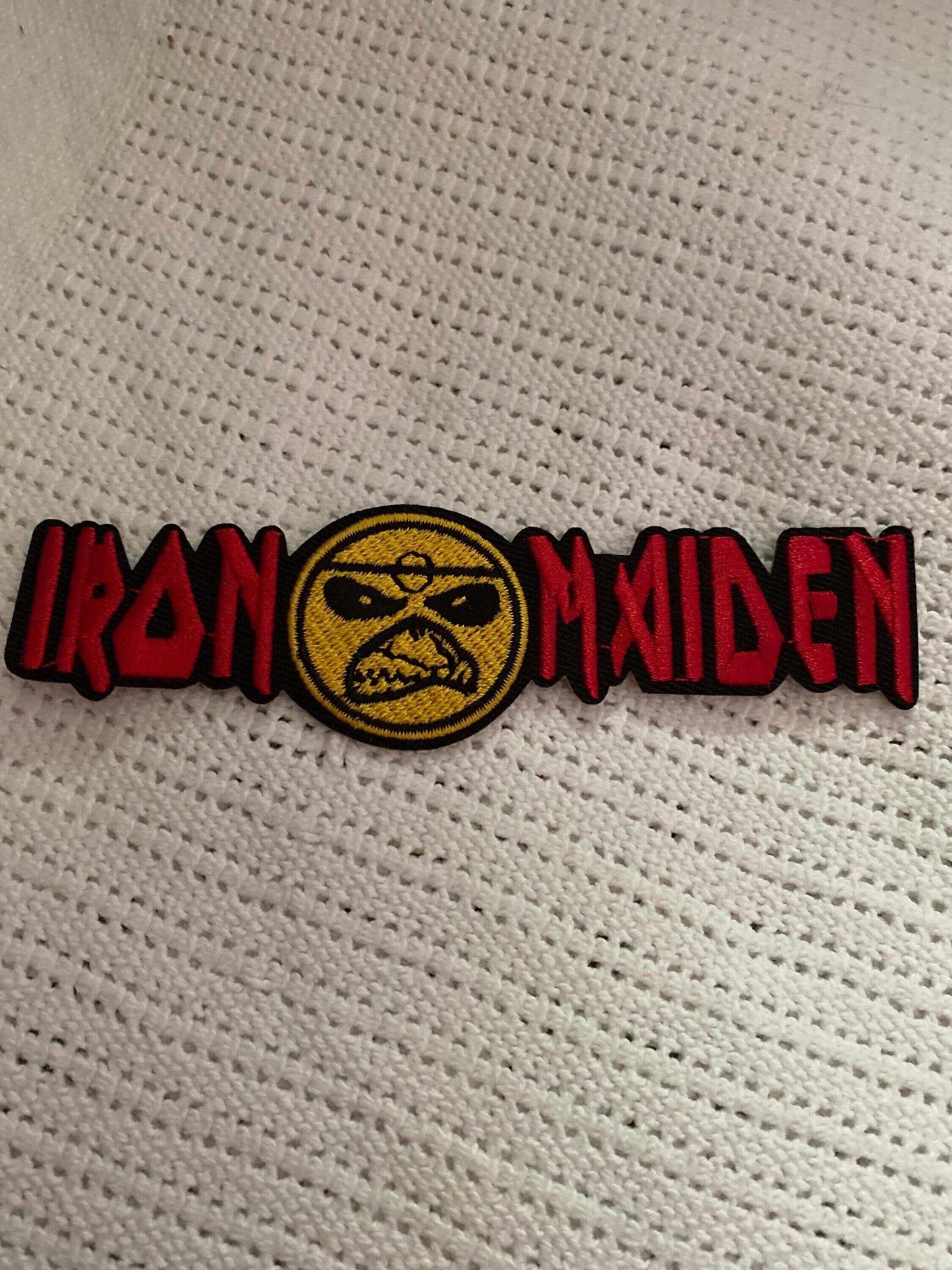 Iron Maiden embroidered patch with red lettering and band mascot face on textured fabric background