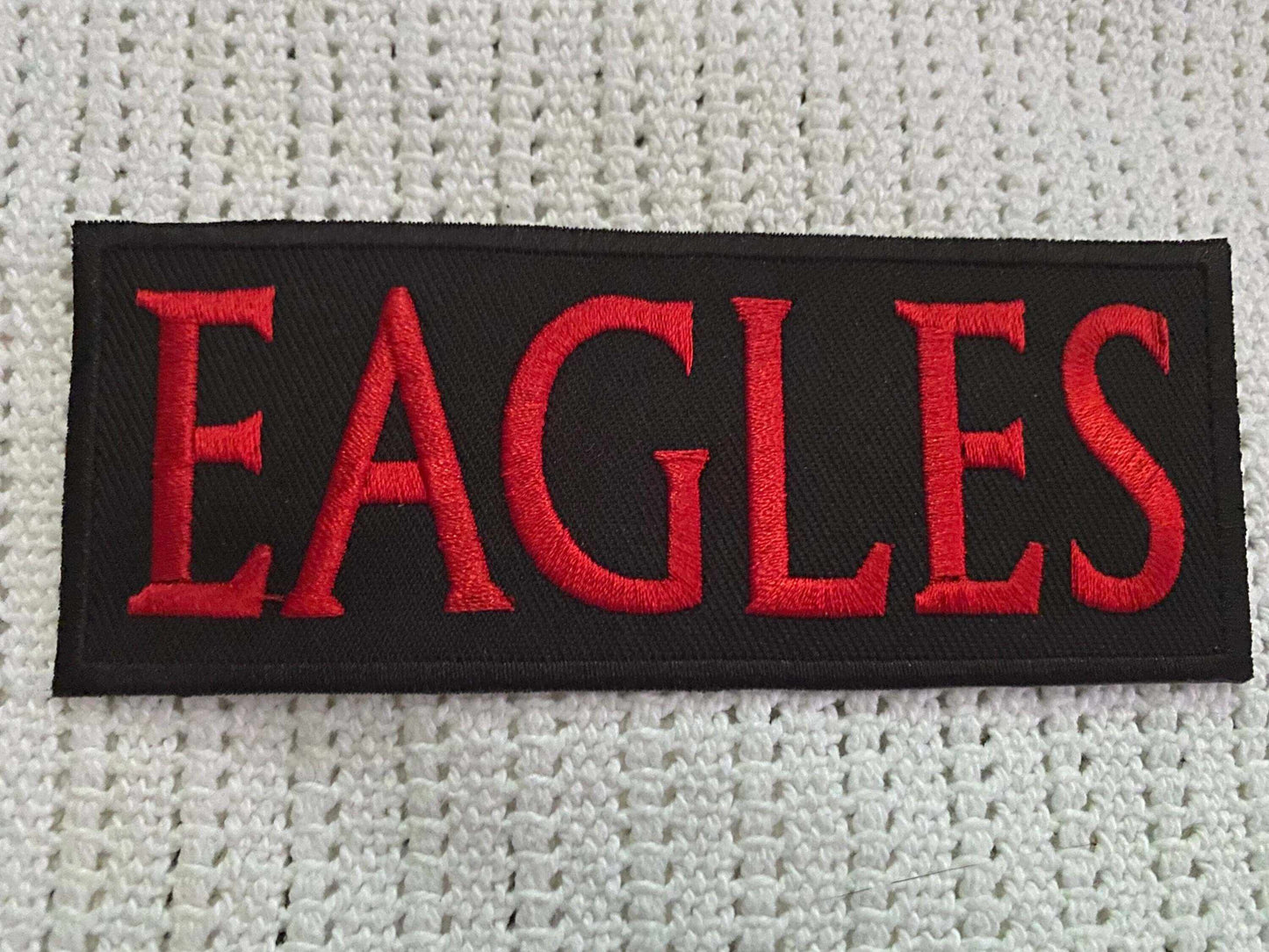 Black patch with bold red embroidered letters spelling "EAGLES" on a white textured fabric background