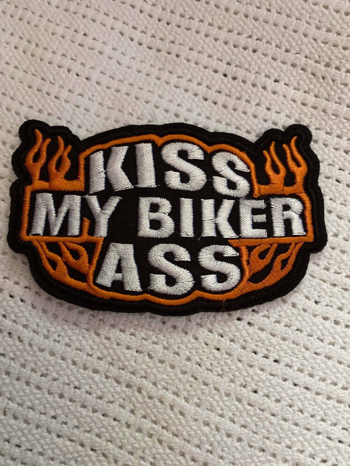 Kiss My Biker Ass embroidered patch with bold white letters and orange flames on black background for biker gear