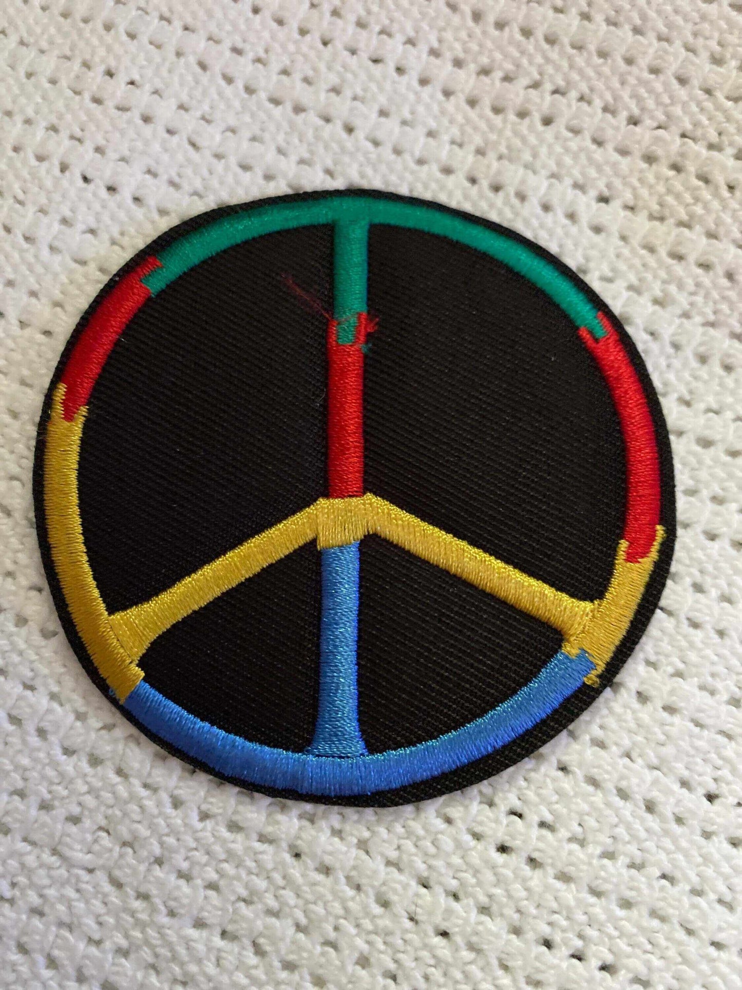 Round patch with a multicolored embroidered peace sign on a black background.