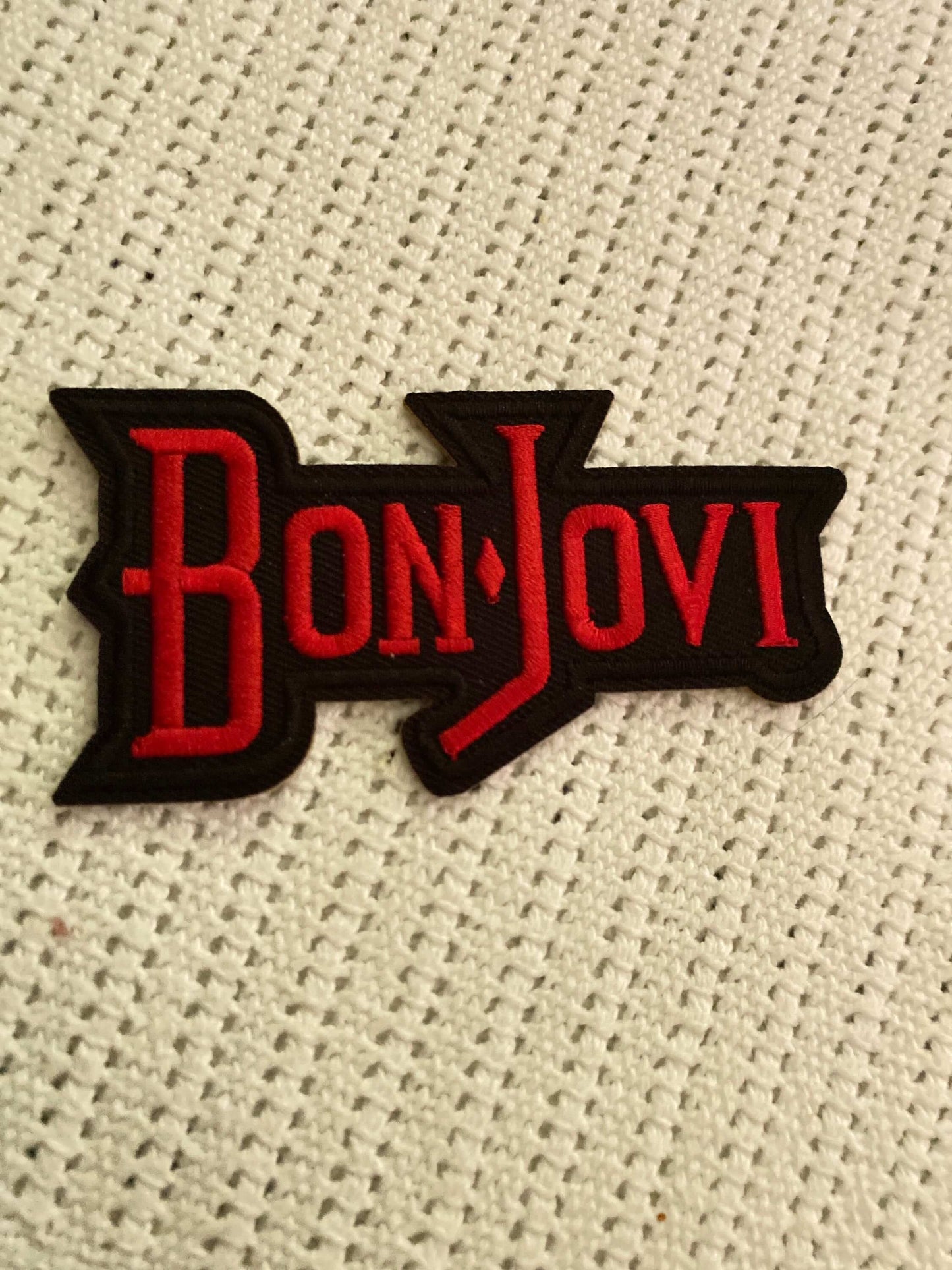 Bon Jovi embroidered patch with red lettering on black background on textured white fabric