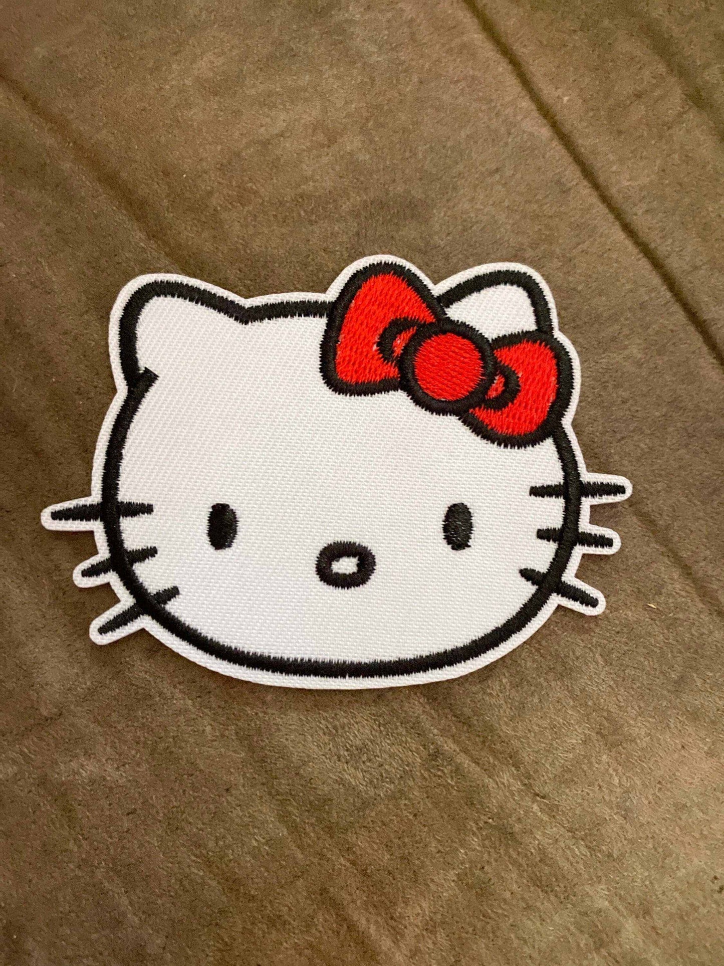 White kitty patch with black outline detailing and a red bow accessory