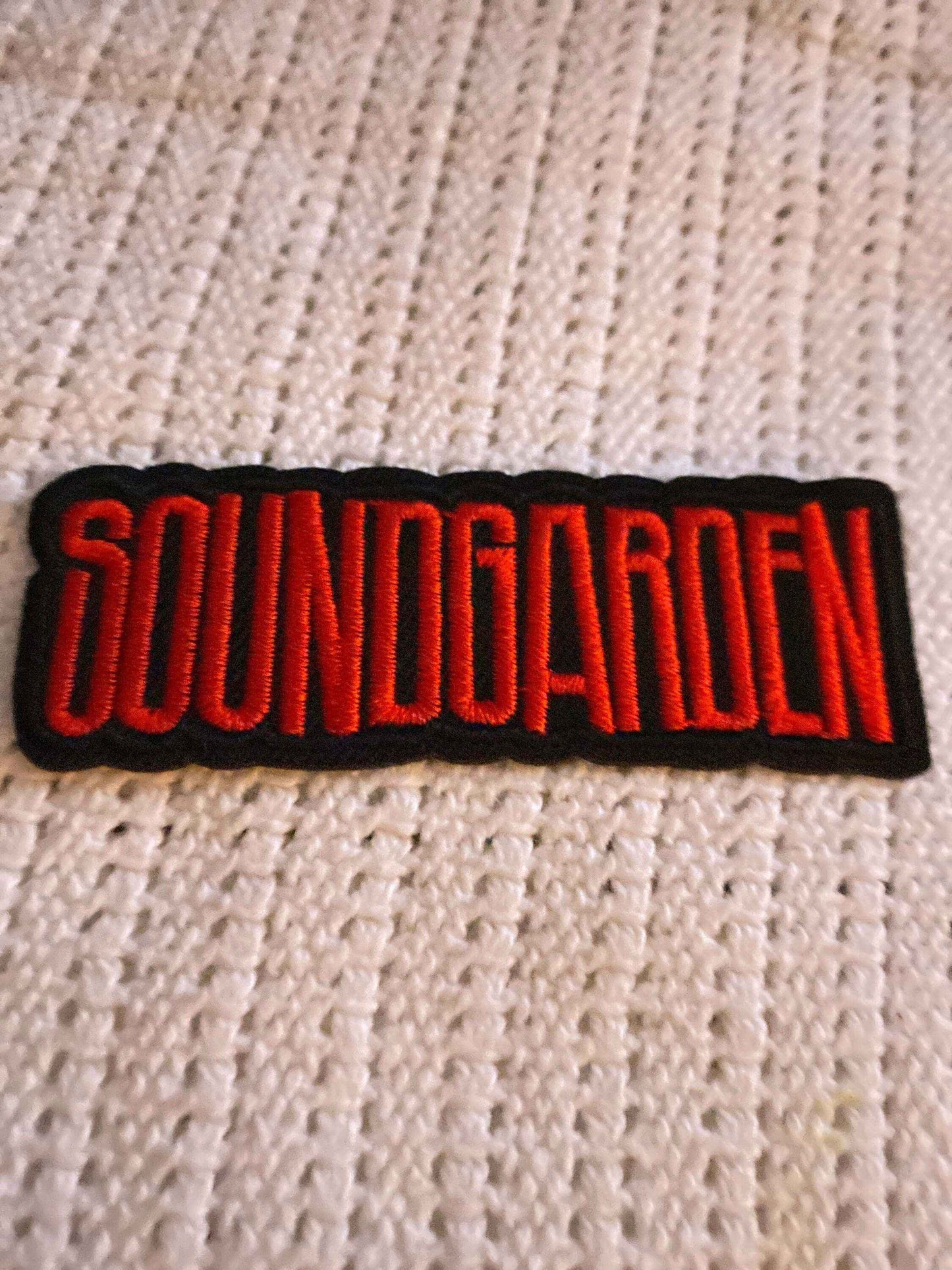 Soundgarden logo embroidered patch in red on black background placed on textured white fabric.