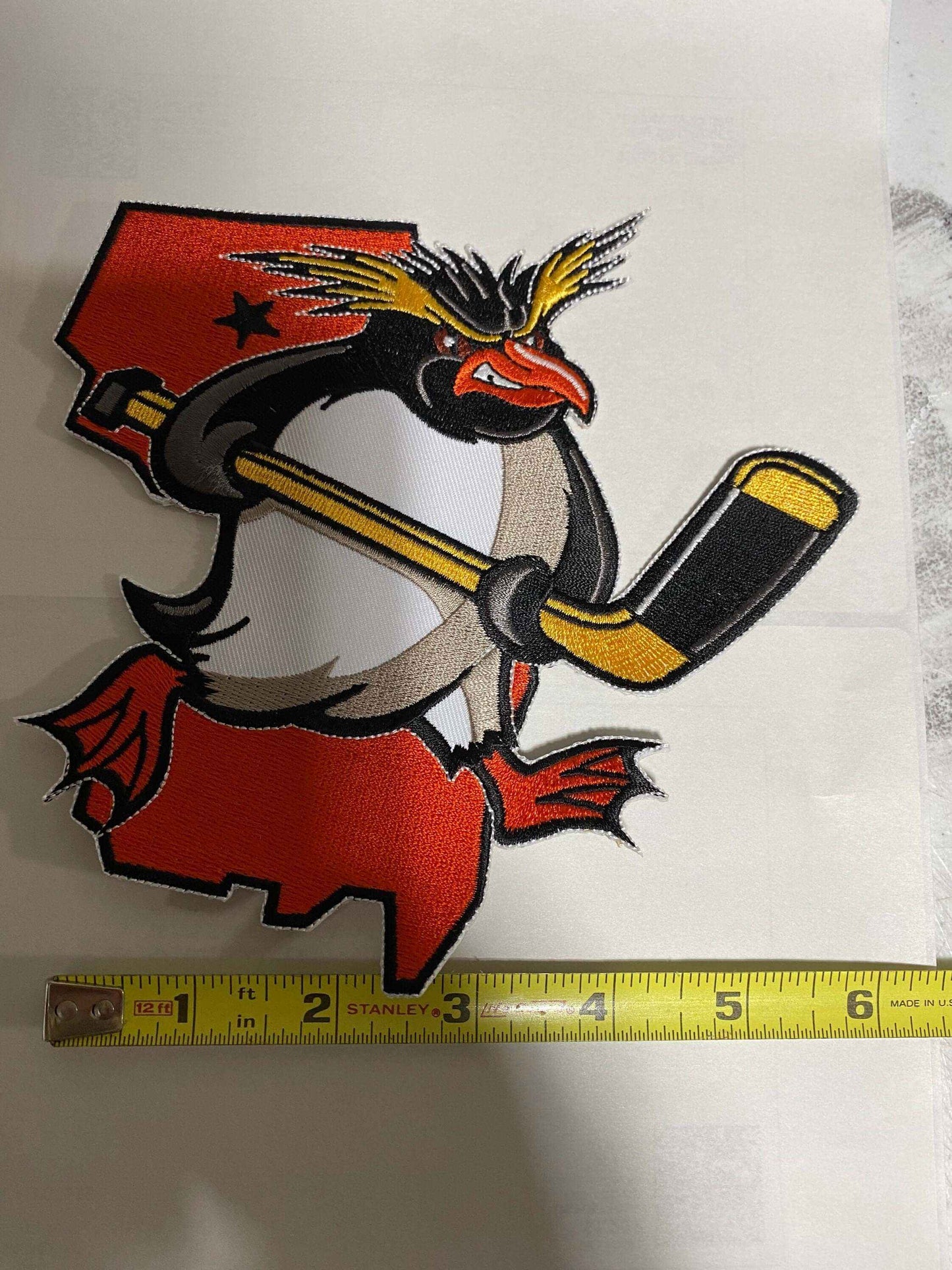 Jersey Rock Hoppers ice hockey team logo featuring a penguin with a hockey stick on a red New Jersey state background