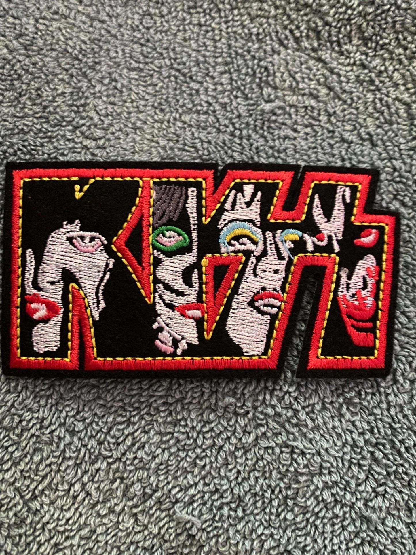 Embroidered KISS logo patch featuring band members' faces inside bold red and black lettering on a gray textured background