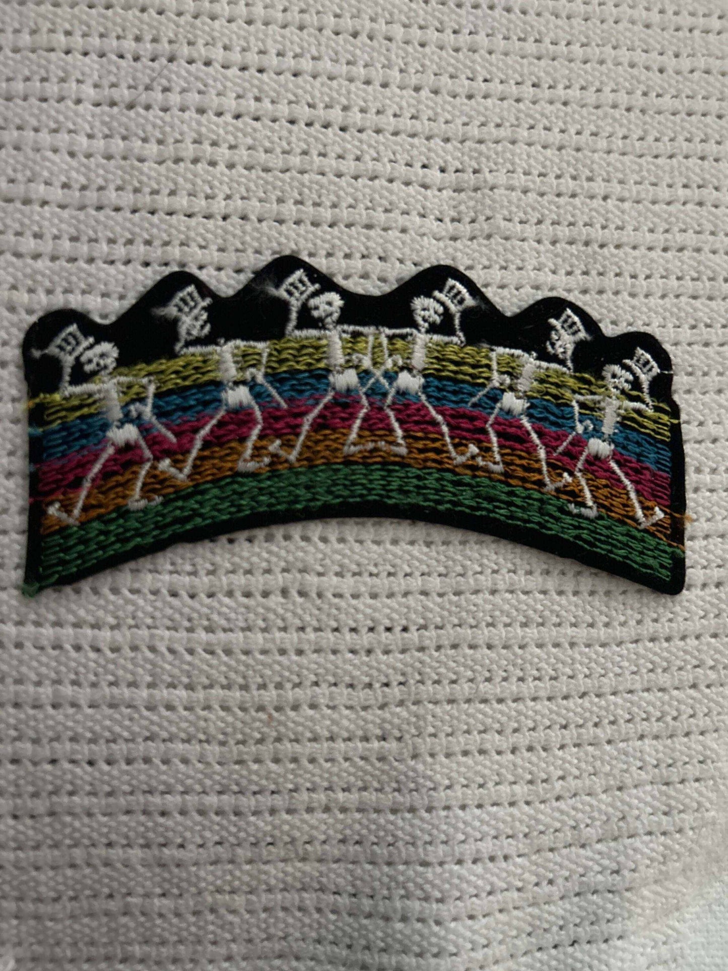 Embroidered patch of Dancing Skeletons Grateful Dead with colorful stripes on a textured white background.