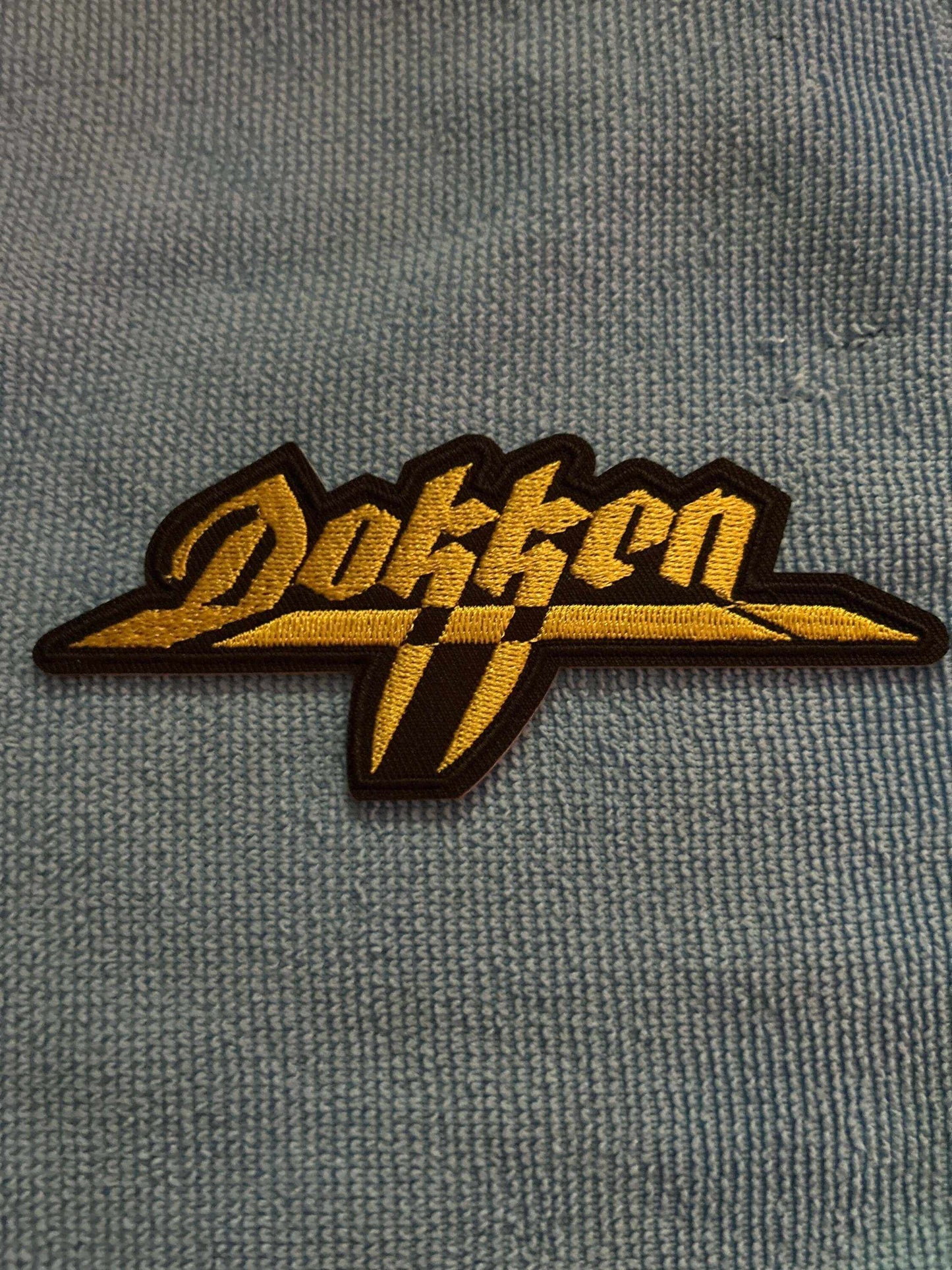 Dokken logo patch with bold yellow lettering on black background for jackets and backpacks